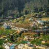 Breathtaking aerial view of terraced fields and homes in Ooty, Tamil Nadu, India, surrounded by lush forest.